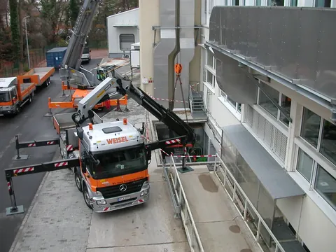 Weisel-Lkw mit Ladekran hebt eine Maschine an einem Gebäude ein